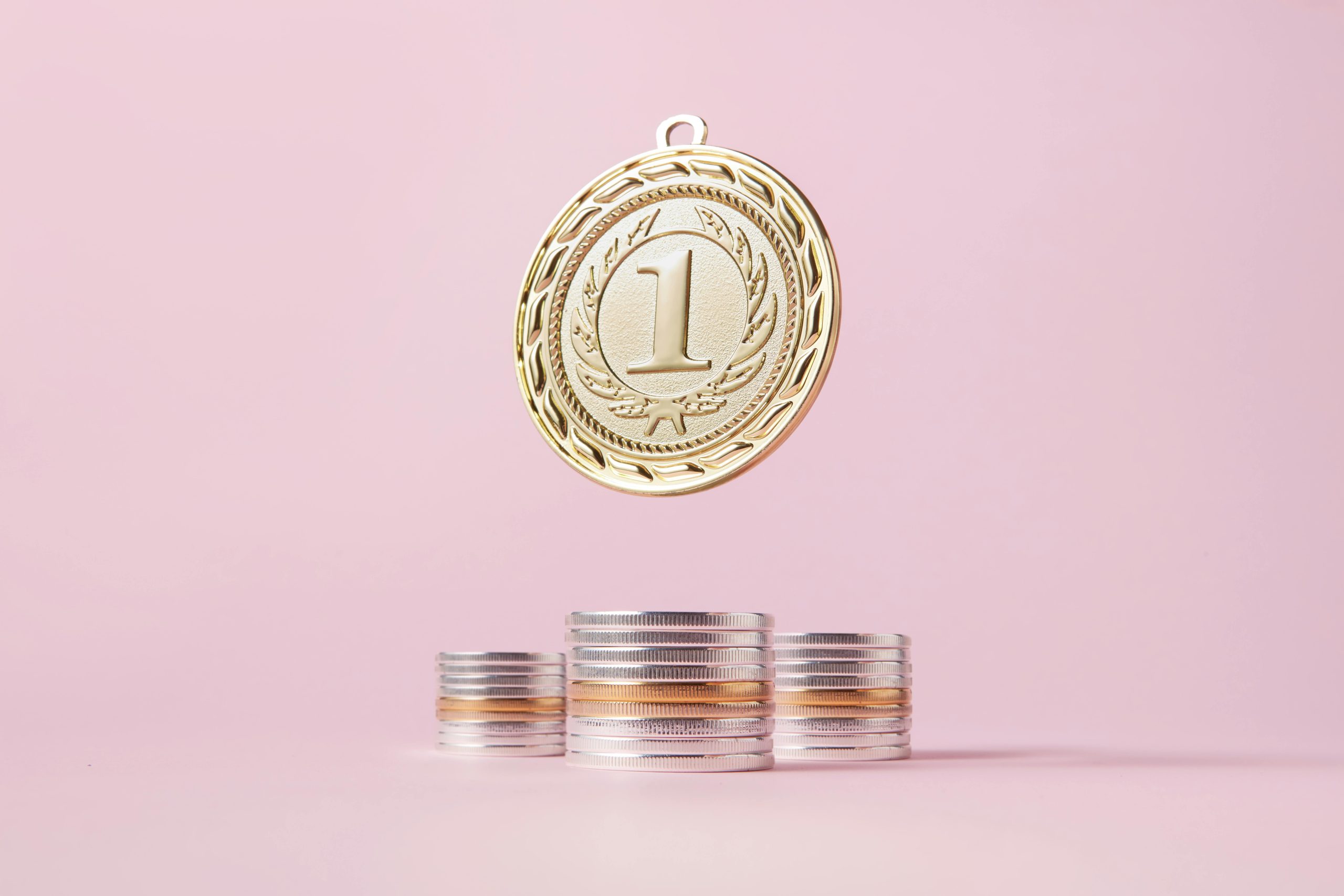 Home A gold medal and stacks of coins on a light pink backdrop, symbolizing victory and wealth.